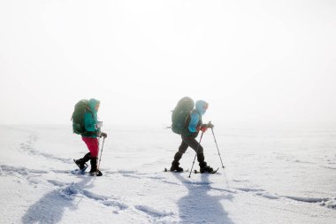 Kış aktivitesi. Karda kar ayakkabılarıyla yürüyen iki kadın, kış yürüyüşü yapan iki kişi, kışın dağlarda yürüyüş yapan iki kişi.
