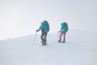 Kar fırtınası sırasında kar ayakkabıları ve sırt çantalı iki kız karda yürür. dağcılık