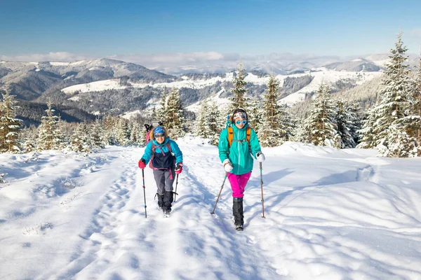 two girls with backpacks walk along a path in the winter mountains. hiking in the mountains. adventure in the mountains