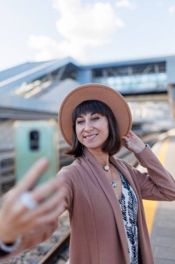 Güzel turist tren istasyonunda selfie çekiyor. Karakolda şapkalı ve ceketli bir kız. seyahat ve macera.