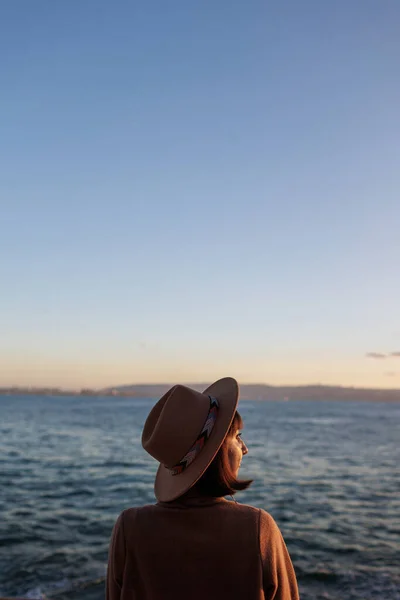 A woman is sailing on a cruise ship, a girl is standing at the fence on a ship and looking at the sea, traveling on a ferry, a brunette in a coat and hat is admiring the ocean. Travel and adventure.