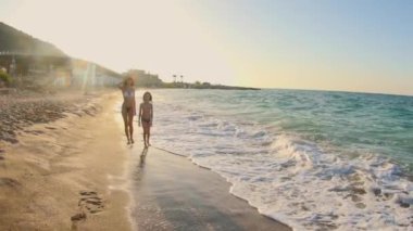 Anne ve oğlu gün batımında kumlu sahil boyunca koşar. Aile tatilinde sahilde. Çocuklarla seyahat etme kavramı.