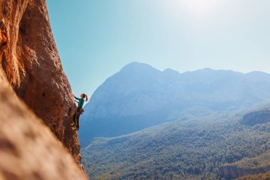 Kız tırmanışçı bir kayaya tırmanır orman ve dağların arka planına karşı. Kaya tırmanışçısı zor bir yolda dinleniyor. Türkiye 'de kaya tırmanışı.