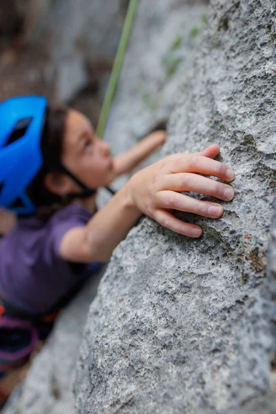 rock climber\'s hand close-up. child rock climber in a blue protective helmet overcomes the route in the mountains. children\'s sports in nature. active time in nature.
