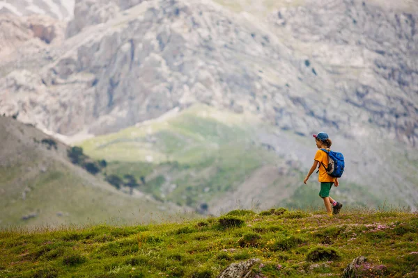 boy with a backpack on a hike against the backdrop of the mountains. child traveler with backpack, hiking, travel, lifestyle concept, mountains in the background, kids summer vacation.