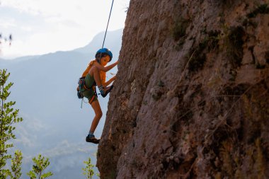 Çocuk doğal bir araziye tırmanıyor. Bir çocuk dağların arka planında bir kayaya tırmanır. Olağanüstü bir hobi. Atletik çocuk güçlü olmayı öğrenir. Kaya tırmanışı güvenli