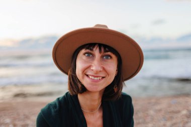 Şapkalı gülümseyen genç bir kızın portresi. Kumsalda oturan mutlu bir gezgin.