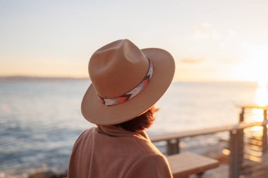 Paltolu ve şapkalı şık ve güzel bir kadın denize bakıyor. Sur boyunca yürü. Denize yakın bir sonbahar. sakinlik ve sükunet.