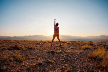Aktif genç bir adam kendini özgür hisseder. Kendine güvenen bir adam gün batımının arka planında bir dağda duruyor. Dağlara git. Doğanın kalbindeki özgürlüğü hisset..