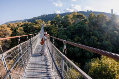 Şapkalı genç kız asma köprüde duruyor ve hayallerindeki uzaklığa bakıyor. yakın plan.