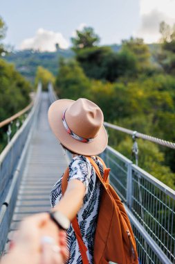 Bir nehrin üzerindeki asma köprüde yürüyen bir kadının sonbahar dönemi açık hava portresi. Kız döndü ve sanki beni takip ediyormuş gibi kameraya elini uzattı. Seyahat ve macera.