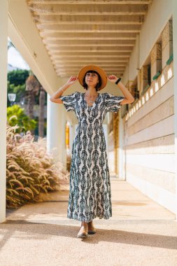 Elbiseli ve şapkalı genç kız caddede yürüyor. Sokakta yürü, güneşli hava, hafta sonu.