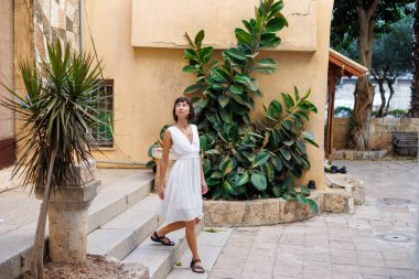 Tatilde bir turist. Özgürlük ve zevk ifade eden bir kadın. Beyaz elbiseli bir kız eski şehrin sokaklarında yürüyor. seyahat ve tatil.