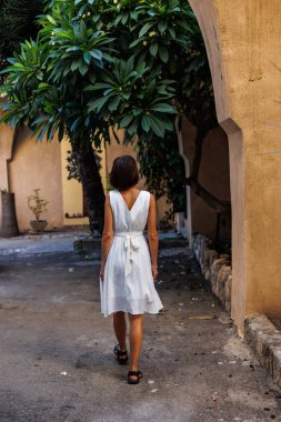 Tatilde bir turist. Bir kadın tatilde şehri gezmekten hoşlanır. Beyaz elbiseli bir kız eski şehrin sokaklarında yürüyor. seyahat ve tatil.