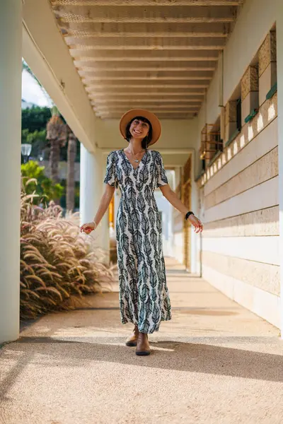 Açık havada, sokakta yürüyen, elbise ve şapka giymiş güzel esmer bir kadının uzun bir portresi. moda ve tarz kavramı.