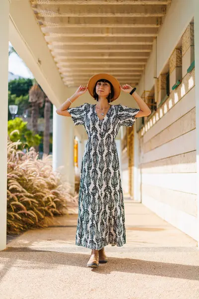 Elbiseli ve şapkalı genç kız caddede yürüyor. Sokakta yürü, güneşli hava, hafta sonu.