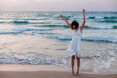 Beyaz bir yaz elbisesi içinde turkuaz denizli tropikal cennet plajının tadını çıkaran mutlu bir gezgin kız. Güzel beyaz elbiseli mutlu genç kadın gün batımında kumsalda yürüyor.. 