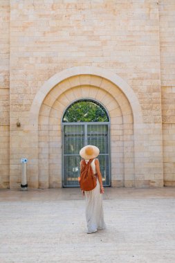 Şapkalı ve sırt çantalı genç bir kız eski binaların arasında yürüyor. İsrail 'de seyahat ve maceralar. Hayfa. Şapkalı güzel kız..