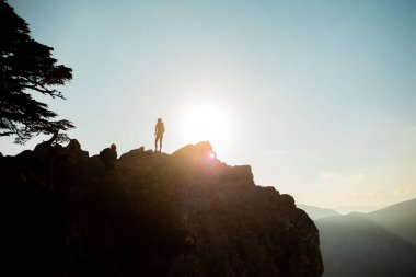 Gün batımında bir kayanın üstünde sırt çantalı bir kızın silueti. Kazananın silueti dağın tepesindeydi. Spor ve aktif yaşam kavramı. dağlarda dolaşmak.