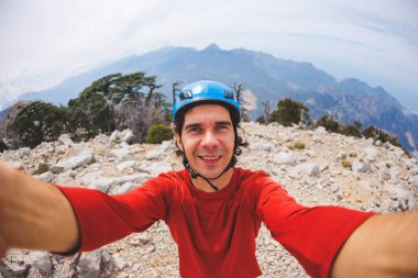 male climber in a helmet takes a selfie photo with the mountains. 