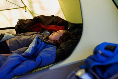 Çocuk bir çadırda yatıyor. Çocuk uyku tulumunda uyuyor. Bir çocukla dağlarda yürüyüş yapmak. etkin yaşam biçimi.