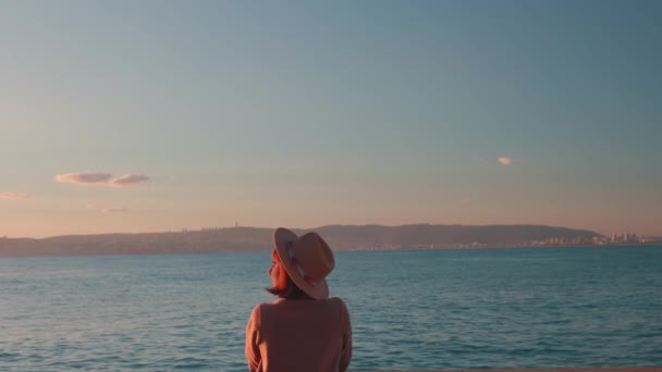 Achteraanzicht Ontspannen Meisje Een Hoed Jas Zittend Voor Zee Stenen — Stockvideo