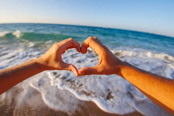 happy young couple showing a heart shape with heart-shaped hands on the background of the sea. Concept of love and infatuation.