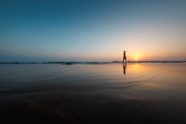 Deniz kıyısında yürüyen bir kadının silueti. Ruhani Barış Meditasyonu. Mutlu bir kız gün batımının arka planında deniz kenarında yürüyor. yan görünüm.