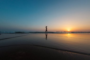 Sahilde yürüyen bir kadının silüeti. Ruhani dünyanın meditasyonu. Mutlu kız gün batımına karşı sahilde yürüyor. yan görünüm.
