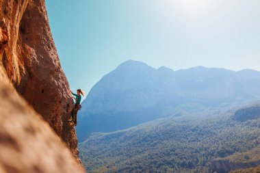 Bir kız kayalara tırmanıyor, bir kaya tırmanışçısı bir dağın arka planına tırmanıyor, sportif bir kız dağa tırmanıyor. Ekstrem. Türkiye.