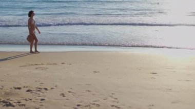 Elinde şapkası olan genç bir kadın kumlu sahilde yürüyor ve tatilin tadını çıkarıyor. Sahilde tatil..