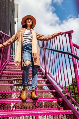 Şehirde şapkalı şık bir kız merdivenlerden aşağı iniyor. Moda tarzı.