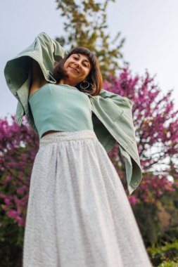 Genç kız şehirde mutlu bir şekilde duruyor. Şık yaz kıyafetleri içinde güzel bir esmerin portresi. Tatil sırasında sokakta gülümseyen neşeli genç bir kadın. Mutlu kız..