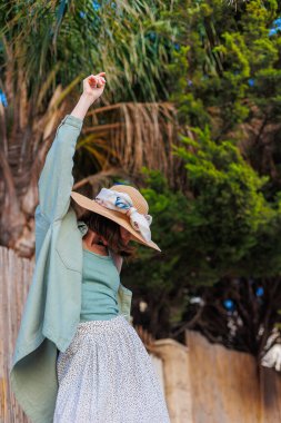 Genç bir esmer şehirde dururken mutlu bir şekilde gülümsüyor. Gömlekli, etekli ve şapkalı şık bir kız avlunun yanında duruyor. Yaz Portresi