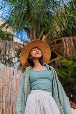 Genç bir esmer şehirde dururken mutlu bir şekilde gülümsüyor. Gömlekli, etekli ve şapkalı şık bir kız avlunun yanında duruyor. Yaz Portresi