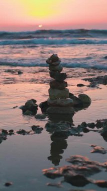 Dikey çekim. Gün batımında sahilde taş dengesi. Sahilde küçük çakıl taşlarından oluşan bir piramit. Gün batımında deniz kenarındaki taşlara karşı. sakinlik ve sükunet kavramı.