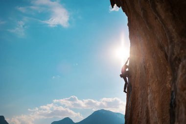 Kaya tırmanışçısı kaya tırmanışı, olimpiyat sporu yapan adam doğal arazi, güç ve dayanıklılık eğitimi, yüksek dağların arka planında kaya tırmanıcısı ve mavi gökyüzü.