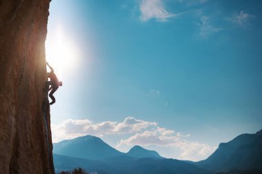 Rock climber climbing rock, man doing olympic sport on natural terrain, strength and endurance training, rock climber on the background of high mountains and blue sky