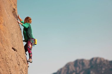 Bir kadın kayaya tırmanıyor. Doğal arazide eğitim. Olağanüstü bir spor. Dağcı doğal bir rahatlama ile antrenman yapar. İpli genç bir kadın kayaya tırmanma sporu için içeri girer..