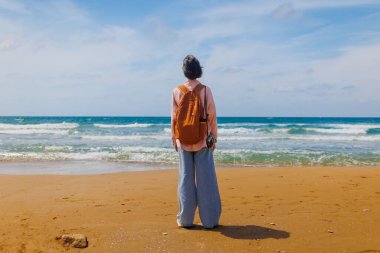 Kameralı kız. Sırt çantalı ve kameralı bayan gezgin sahilde duruyor ve tatil boyunca deniz manzarasının tadını çıkarıyor. macera ve seyahat.