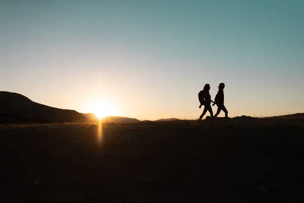 Silhouette Two Girls Backpacks While Traveling Mountains Sunset Two People lizenzfreie Stockbilder