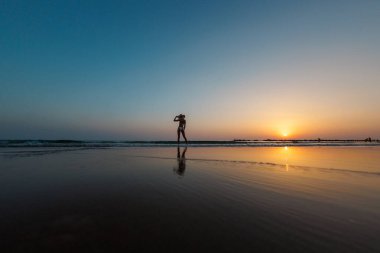Sahilde yürüyen bir kadının silüeti. Ruhani dünyanın meditasyonu. Mutlu kız gün batımına karşı sahilde yürüyor. yan görünüm.