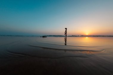 Gün batımında sahilde yürüyen mutlu kız. Sahilde yürüyen bir kadının silüeti. Kumsalda dinlenmek. yan görünüm.