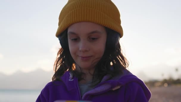 Chłopiec Noszący Słuchawki Stoi Plaży Wybiera Piosenkę Słuchania Przez Telefon Filmik Stockowy