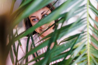 Yüzünde palmiye yaprağı gölgeleri olan güzel bir kadının yakın plan portresi. Doğal güzellik, tropik yaprakların arka planına karşı. Güzel yaz kızı palmiye yapraklarının arkasında.