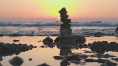 Kumsalda dinlenmek. Sahilde küçük çakıl taşlarından oluşan bir piramit. Gün batımında deniz kenarındaki taşlara karşı. Gün batımında sahilde taş dengesi..