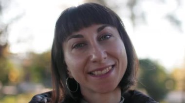 Kız gülümsüyor. Kısa esmer saçlı, neşeli, güzel bir kız. Açık havada poz vermek. Deri ceket, sokak tarzında yakın plan moda portresi..