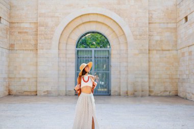 Şapkalı ve sırt çantalı genç bir kız eski binaların arasında yürüyor. İsrail 'de seyahat ve maceralar. Hayfa. Şapkalı güzel kız..