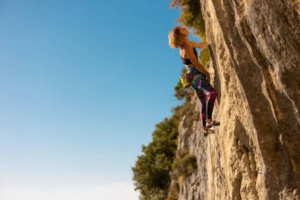 少女は岩に登る 登山列車は自然の地形を利用している 青い空を背景に困難な登山ルートを克服する女性 ストック写真