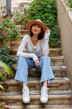 Şapkalı genç kız çiçeklerin yanındaki basamaklarda oturuyor. Şehir tarzı. Sonbahar konsepti.